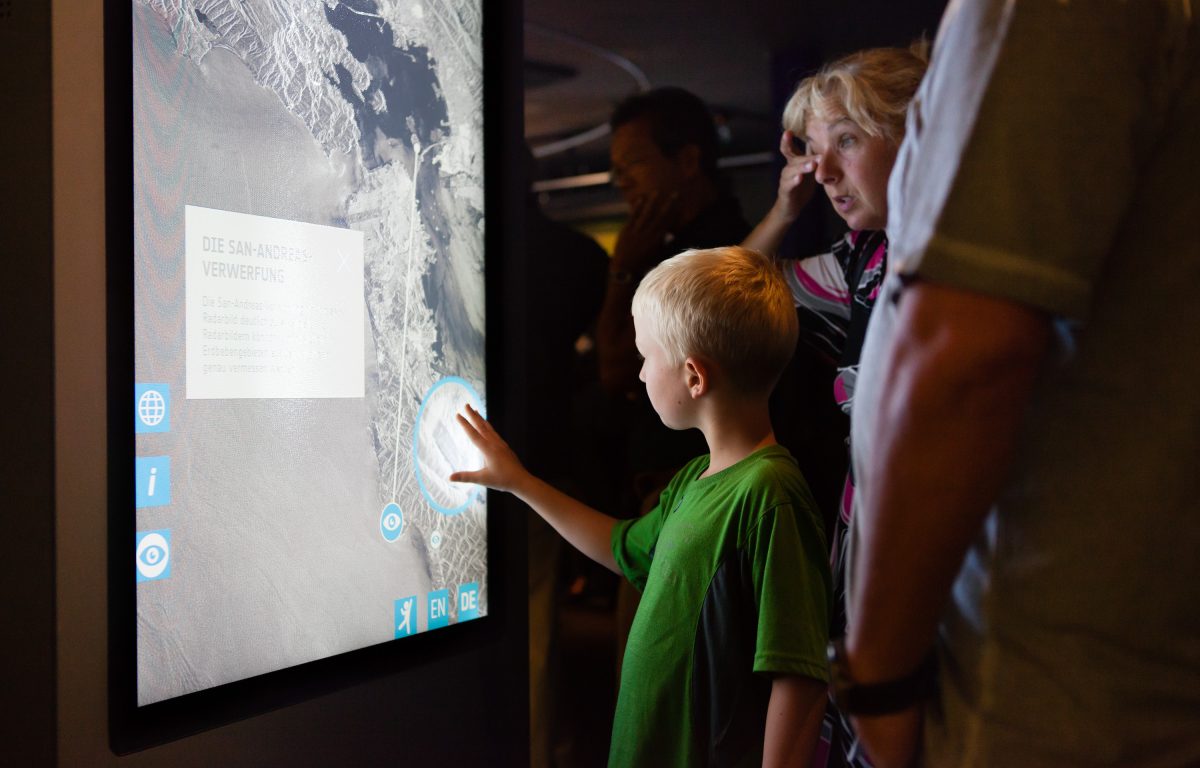 Child touching the multitouch screen of a multitouch stele in the exhibition